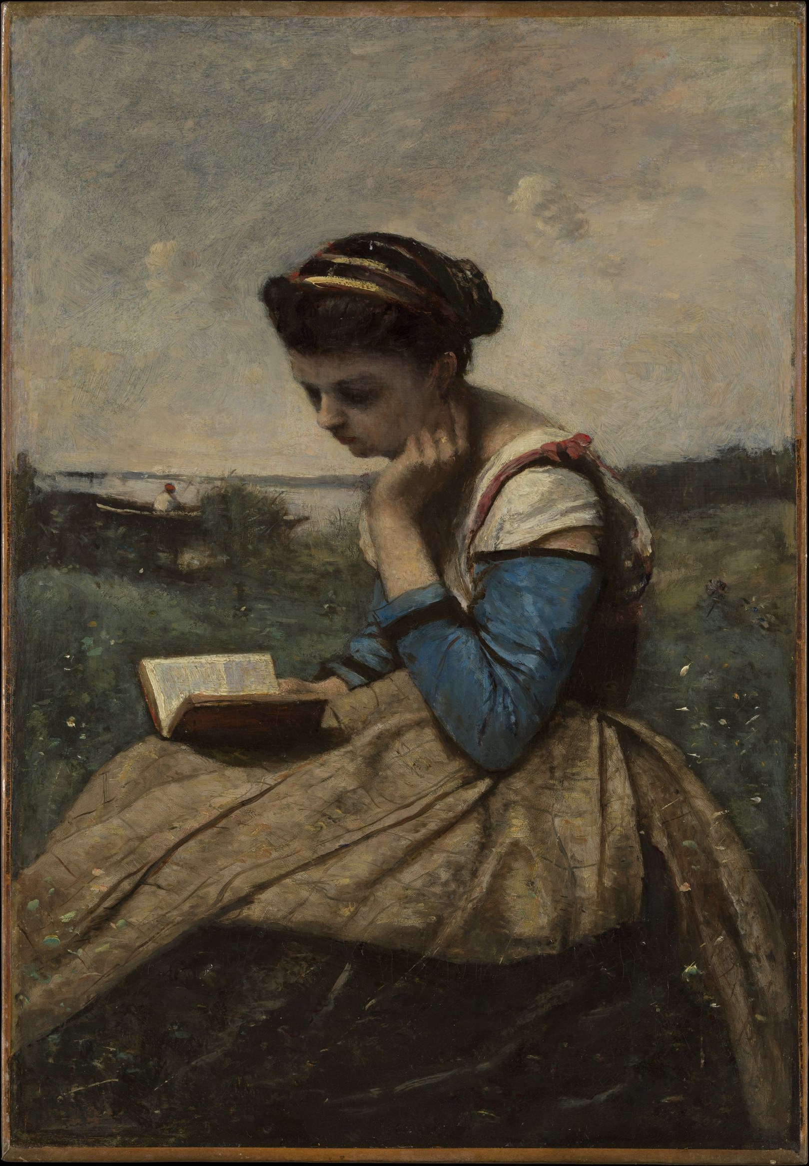 屋外で座った女性が、膝に置いた本へ目を落としている。