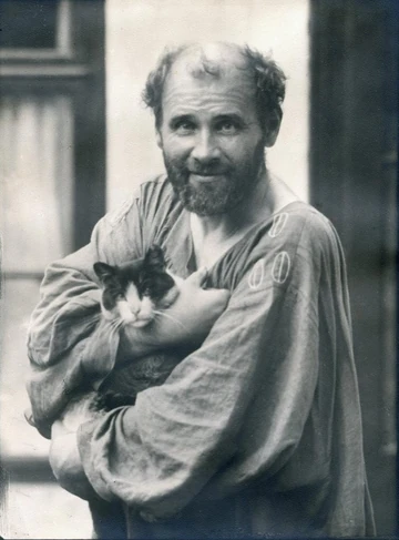 白い仕事着を着て猫を抱くグスタフ・クリムト。モーリツ・ネーアが1910年に撮影した肖像写真。